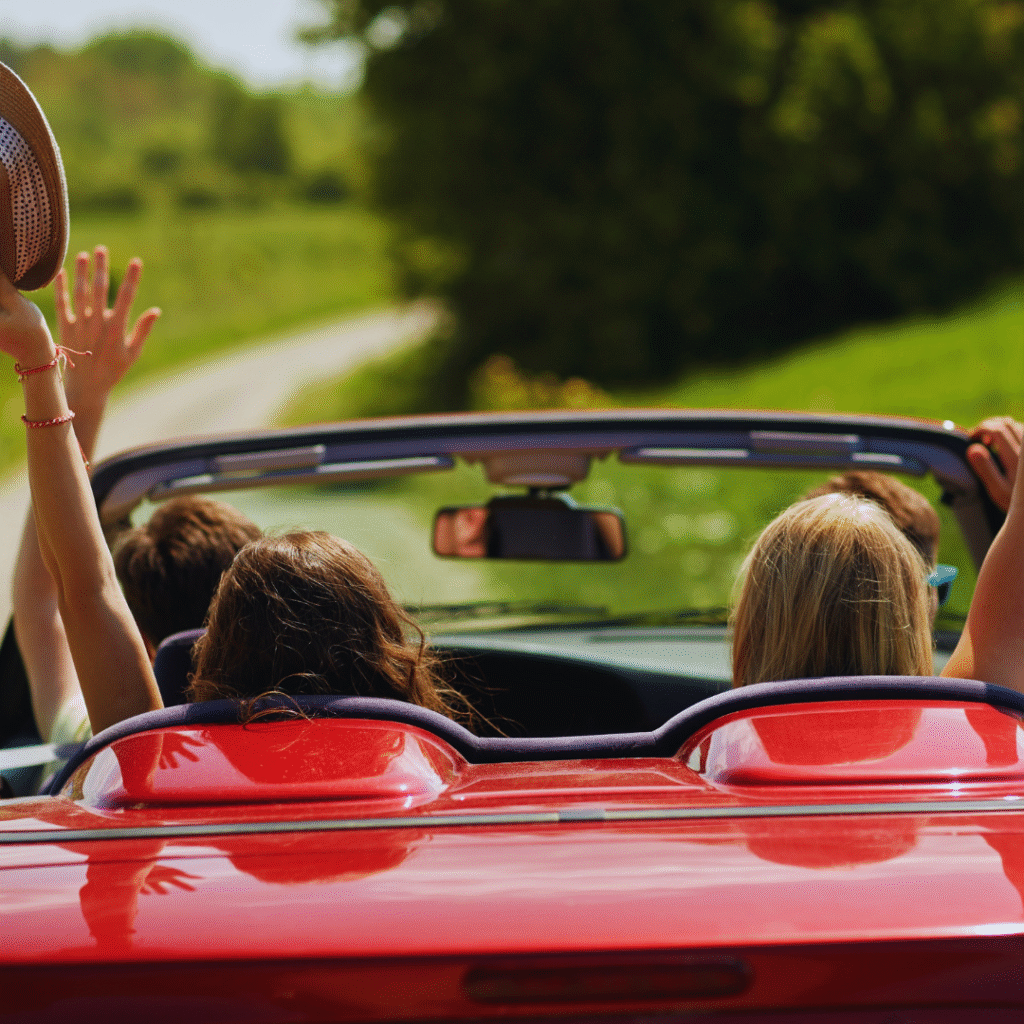 Red car on the road, its hood down, people celebrating the road ahead.
